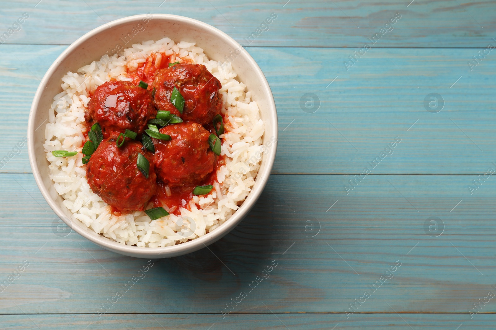 Photo of Tasty meatballs with sauce and rice on light blue wooden table, top view. Space for text