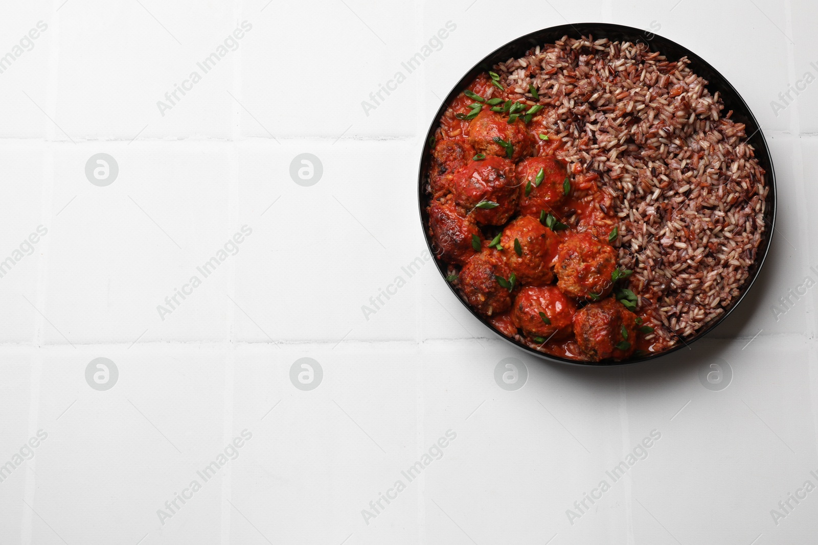 Photo of Tasty meatballs with sauce and brown rice on white tiled table, top view. Space for text