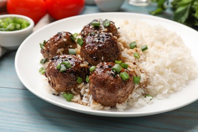 Photo of Delicious rice with meatballs, sauce and green onions on blue wooden table, closeup