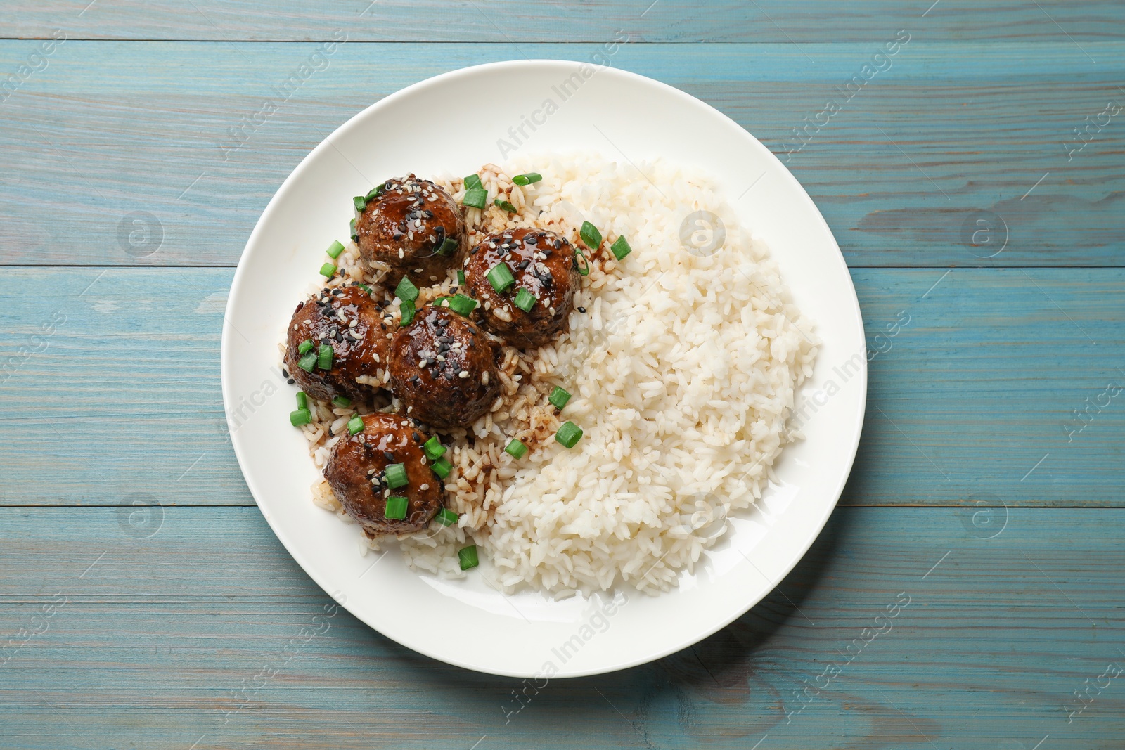 Photo of Delicious rice with meatballs, sauce and green onions on blue wooden table, top view