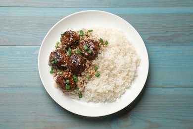 Photo of Delicious rice with meatballs, sauce and green onions on blue wooden table, top view