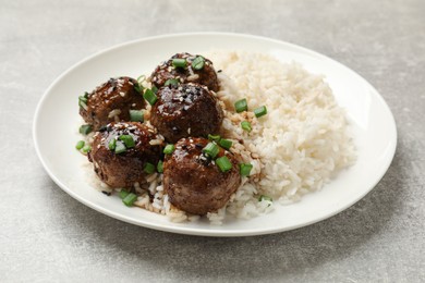 Photo of Delicious rice with meatballs, sauce and green onions on grey table, closeup