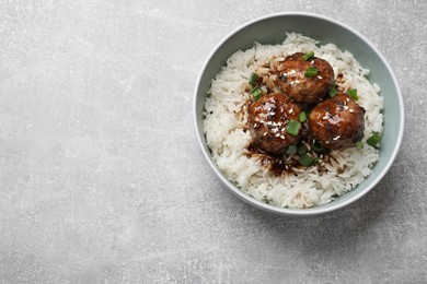 Photo of Delicious rice with meatballs, sauce and green onions in bowl on grey table, top view. Space for text