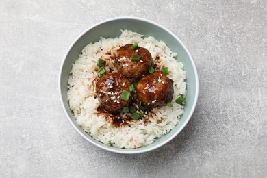 Photo of Delicious rice with meatballs, sauce and green onions in bowl on grey table, top view