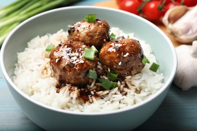 Photo of Delicious rice with meatballs, sauce and green onions on blue wooden table, closeup