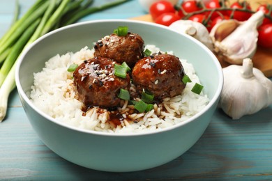 Photo of Delicious rice with meatballs, sauce and green onions on blue wooden table, closeup