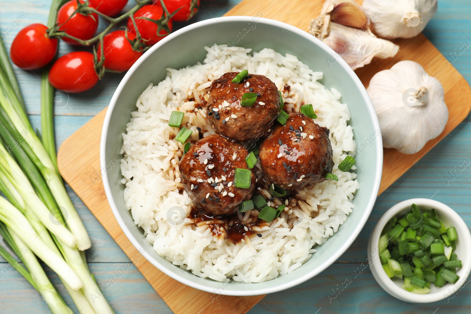 Photo of Delicious rice with meatballs, sauce and green onions on blue wooden table, flat lay