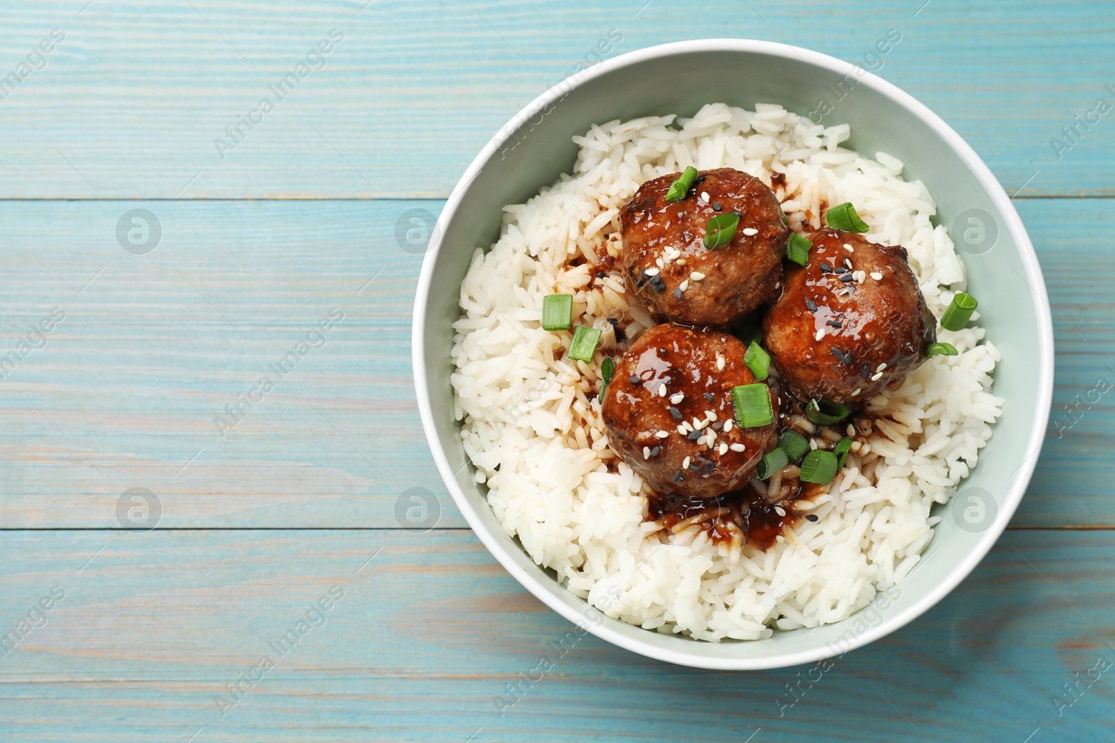 Photo of Delicious rice with meatballs, sauce and green onions in bowl on blue wooden table, top view. Space for text