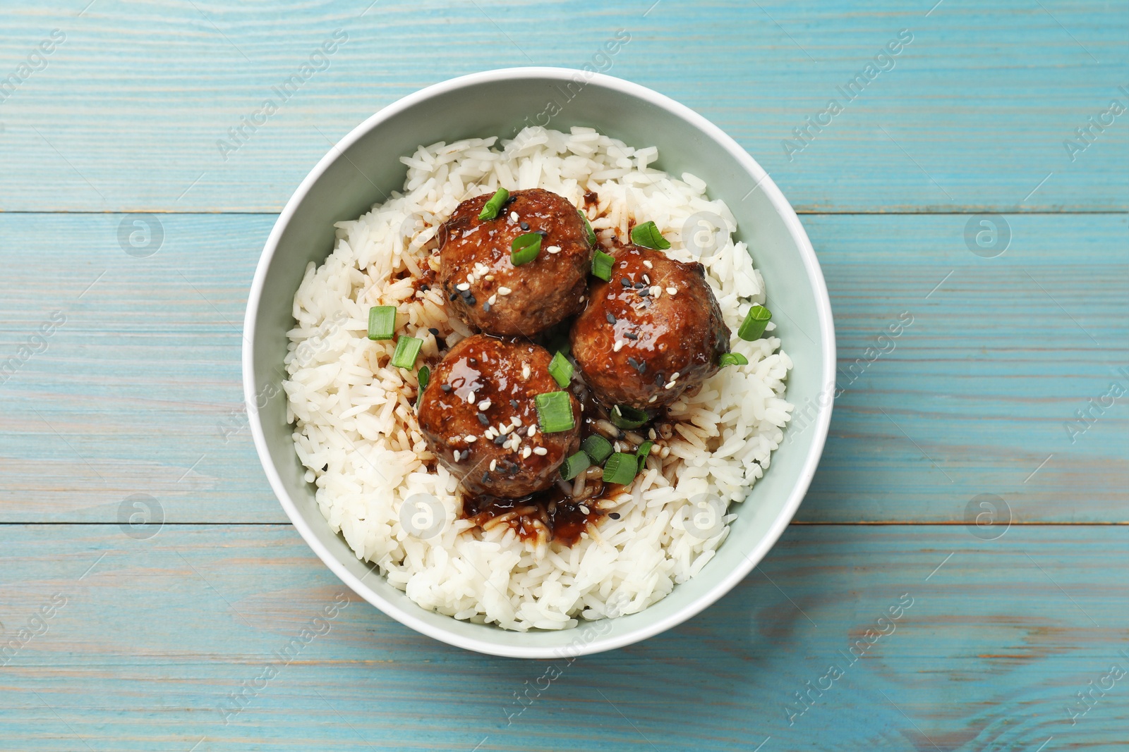 Photo of Delicious rice with meatballs, sauce and green onions in bowl on blue wooden table, top view