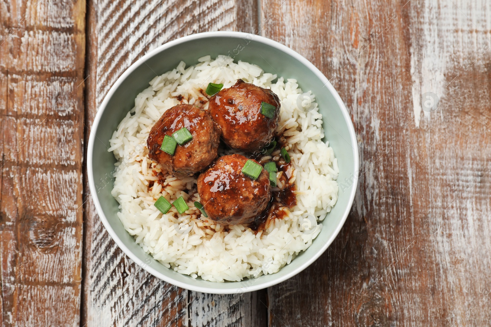 Photo of Delicious rice with meatballs, sauce and green onions in bowl on wooden table, top view