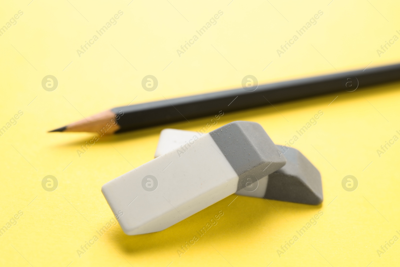 Photo of Erasers and pencil on yellow background, closeup