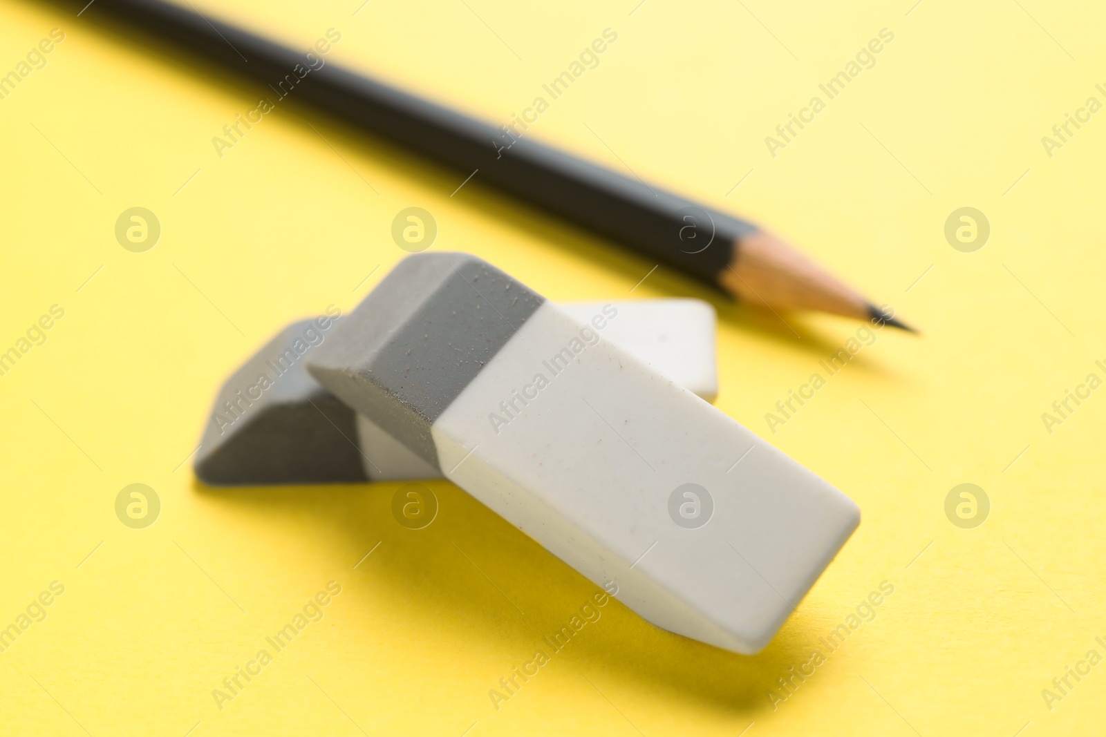 Photo of Erasers and pencil on yellow background, closeup