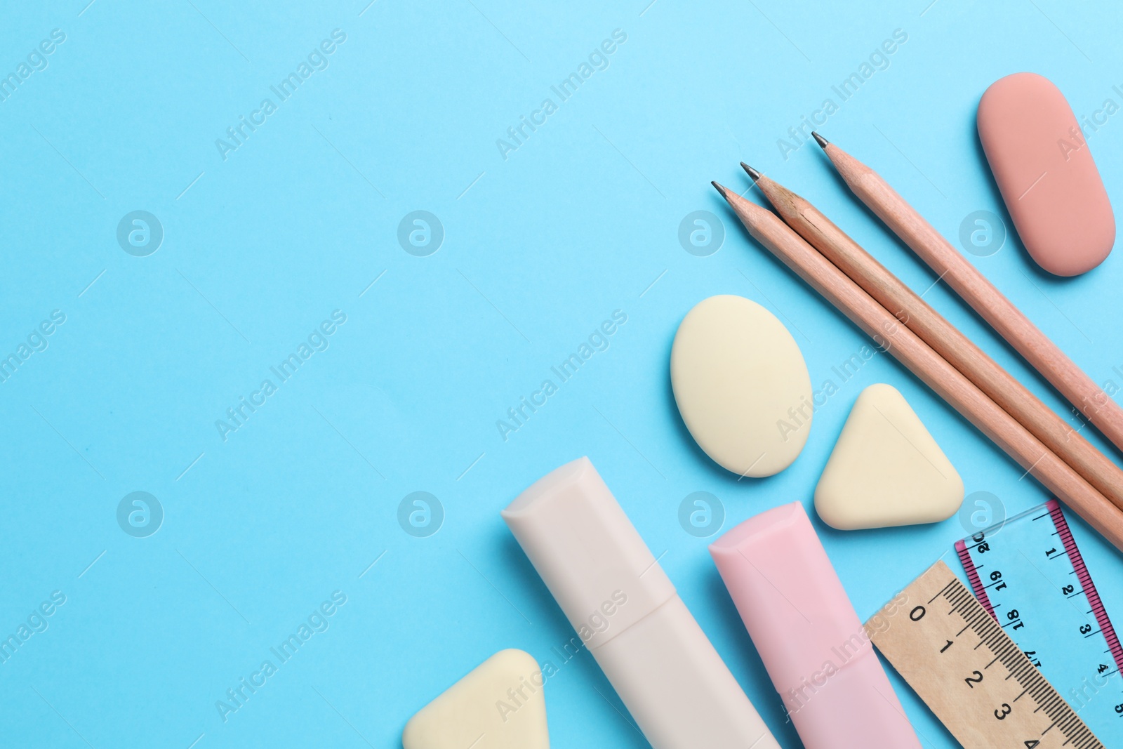 Photo of Erasers and other stationery on light blue background, flat lay. Space for text