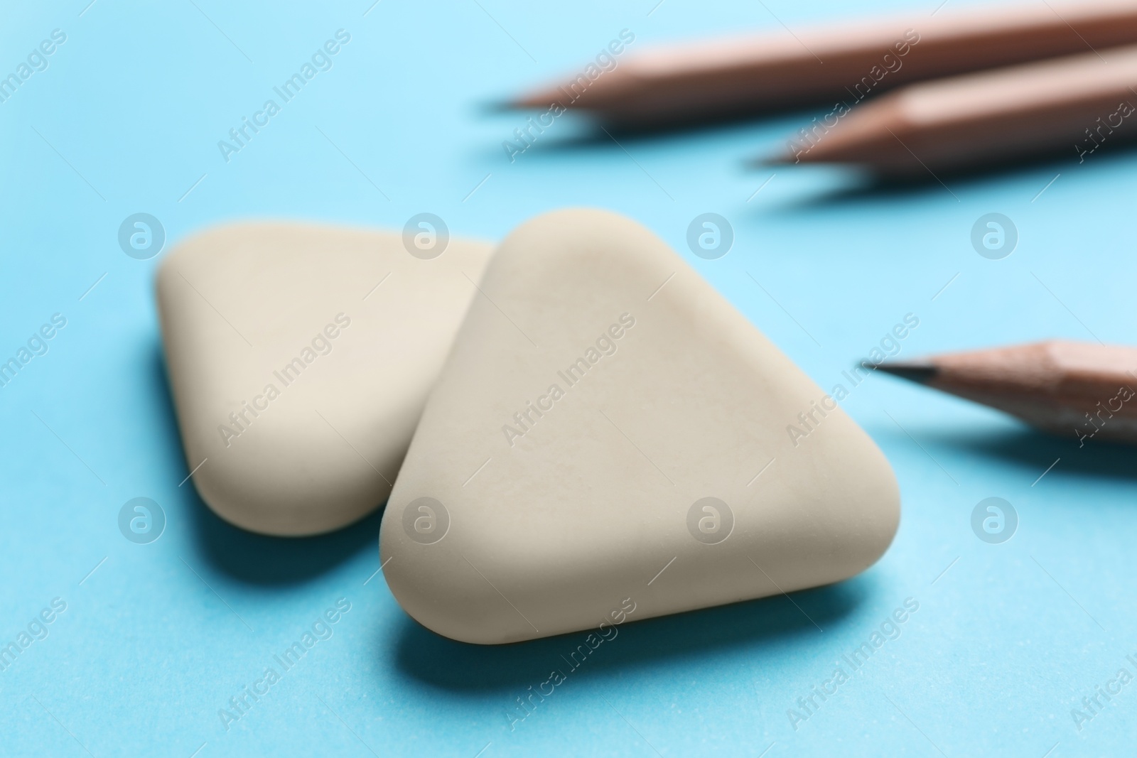 Photo of Erasers and pencils on light blue background, selective focus