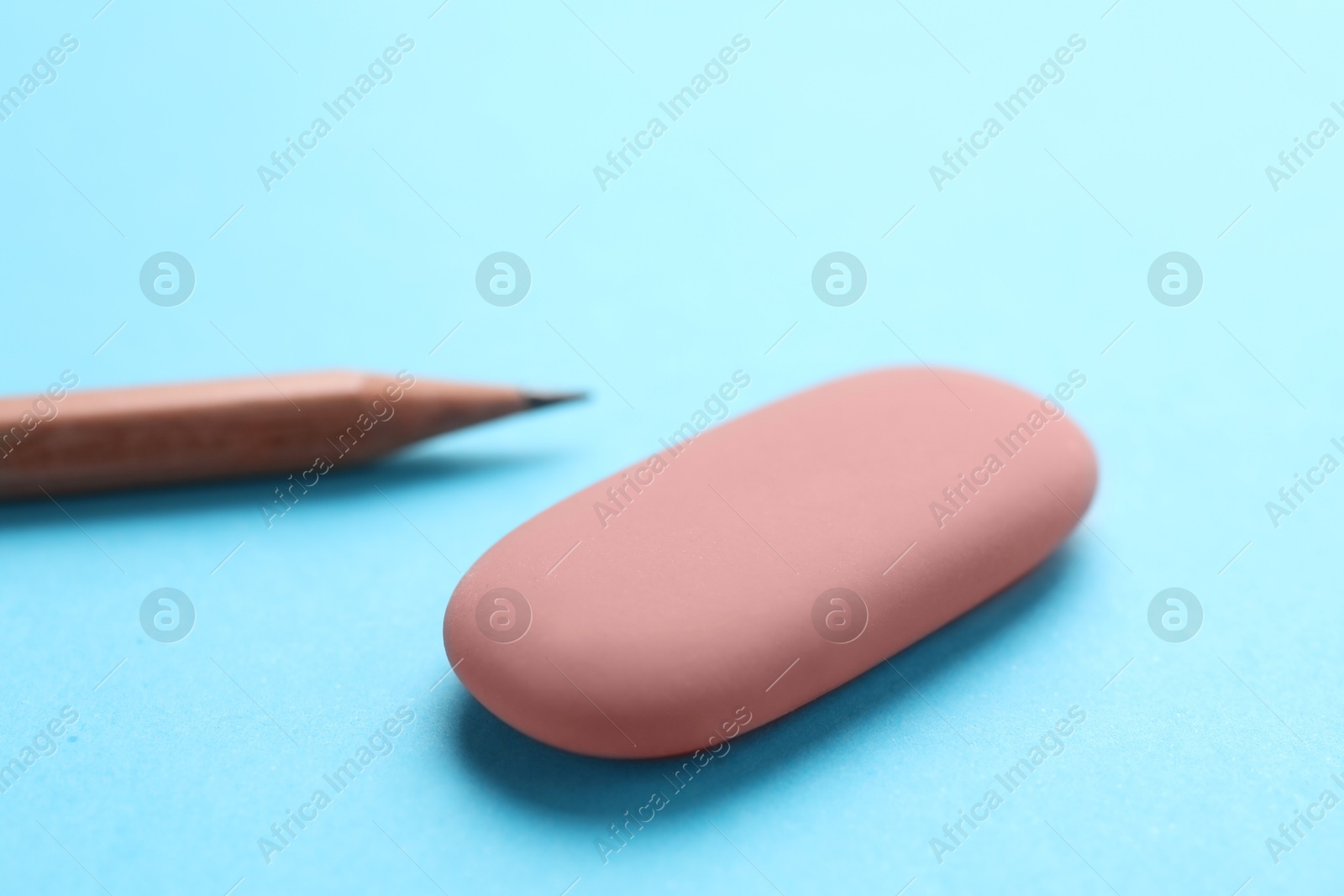 Photo of Eraser and pencil on light blue background, closeup