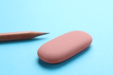 Photo of Eraser and pencil on light blue background, closeup