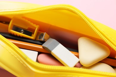 Photo of Erasers and other different stationery in pencil case on pink background, closeup