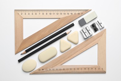 Photo of Erasers, pencils, triangle rulers and sharpeners on white background, flat lay