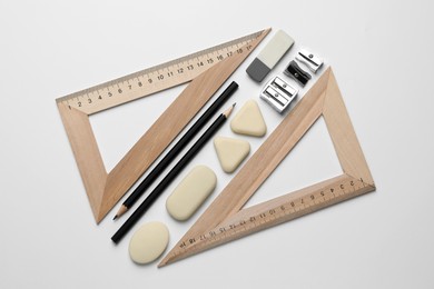 Photo of Erasers, pencils, triangle rulers and sharpeners on white background, flat lay