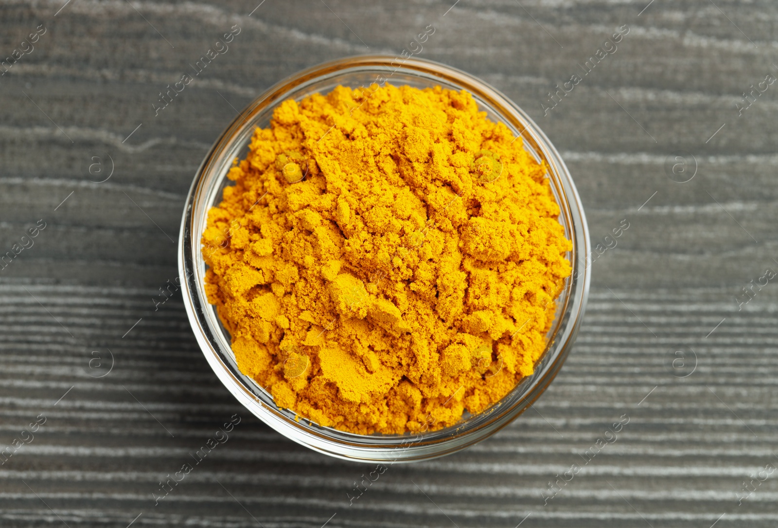 Photo of Turmeric powder in glass bowl on grey wooden table, top view