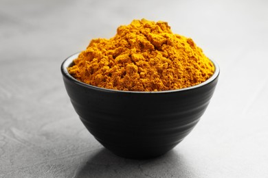 Photo of Turmeric powder in bowl on grey table, closeup