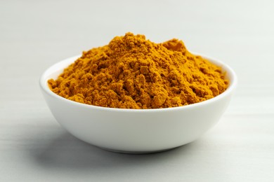 Photo of Turmeric powder in bowl on white table, closeup