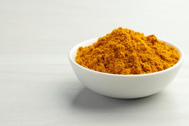 Photo of Turmeric powder in bowl on white table, closeup. Space for text