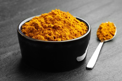 Photo of Turmeric powder in bowl and spoon on grey table, closeup