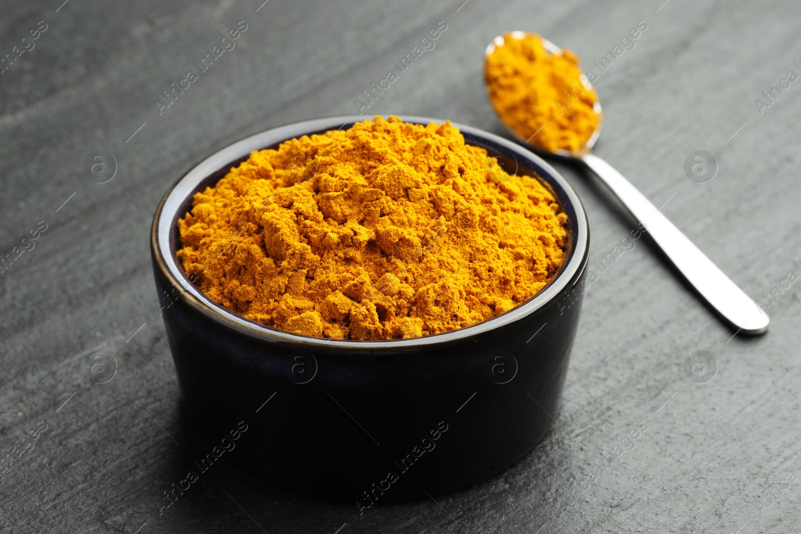 Photo of Turmeric powder in bowl and spoon on grey table, closeup