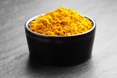 Photo of Turmeric powder in bowl on grey table, closeup