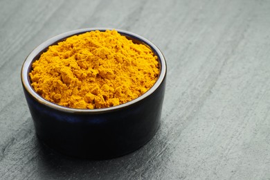 Photo of Turmeric powder in bowl on grey table, closeup. Space for text