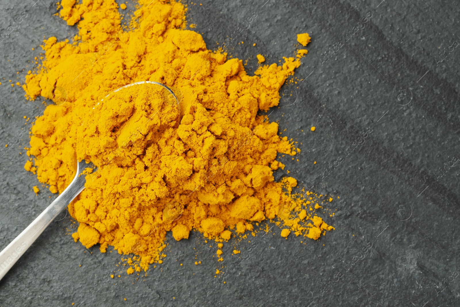 Photo of Turmeric powder and spoon on grey table, top view. Space for text