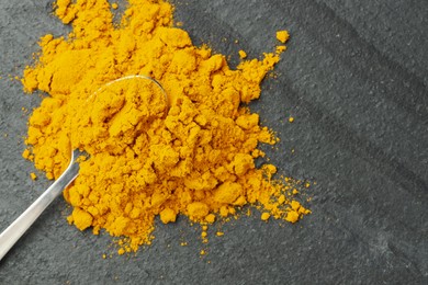 Photo of Turmeric powder and spoon on grey table, top view. Space for text