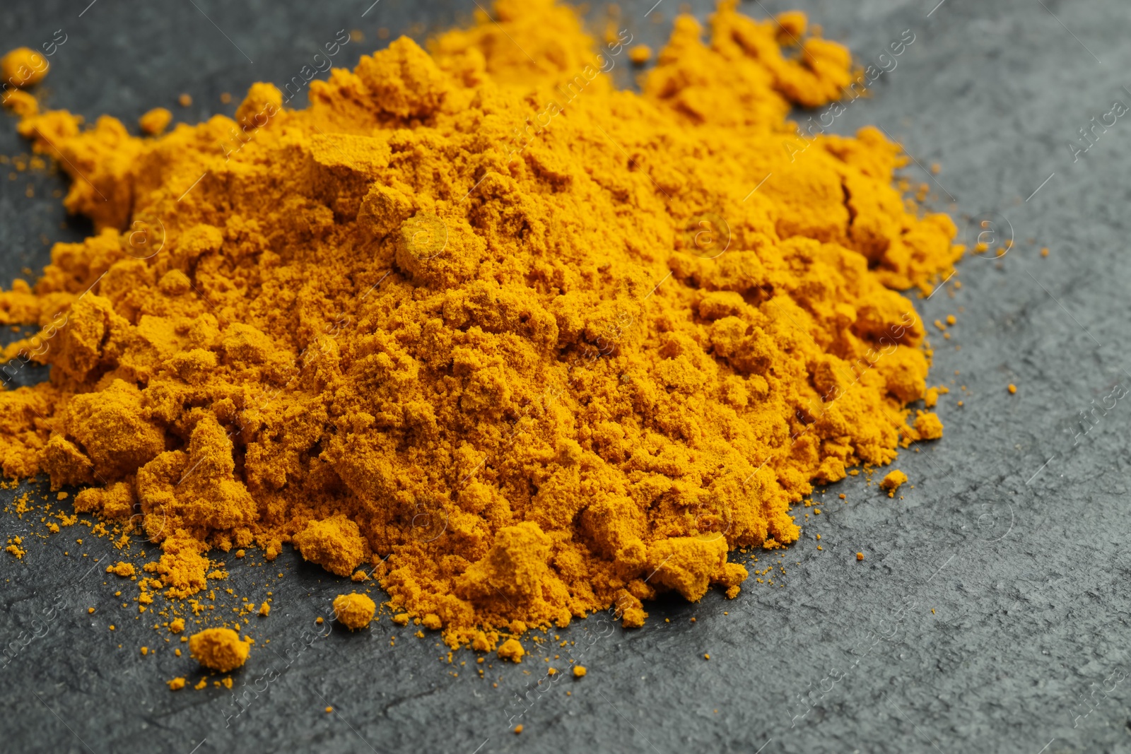 Photo of Heap of turmeric powder on grey table, closeup