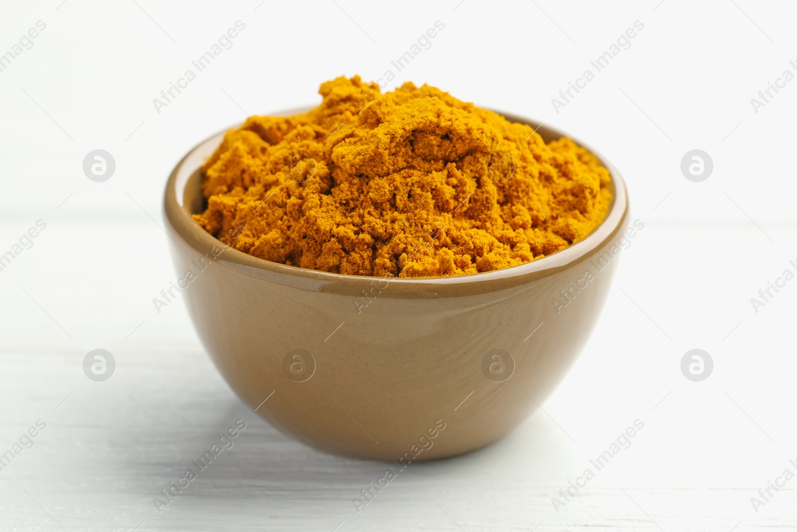 Photo of Turmeric powder in bowl on white wooden table, closeup