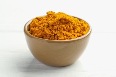 Photo of Turmeric powder in bowl on white wooden table, closeup