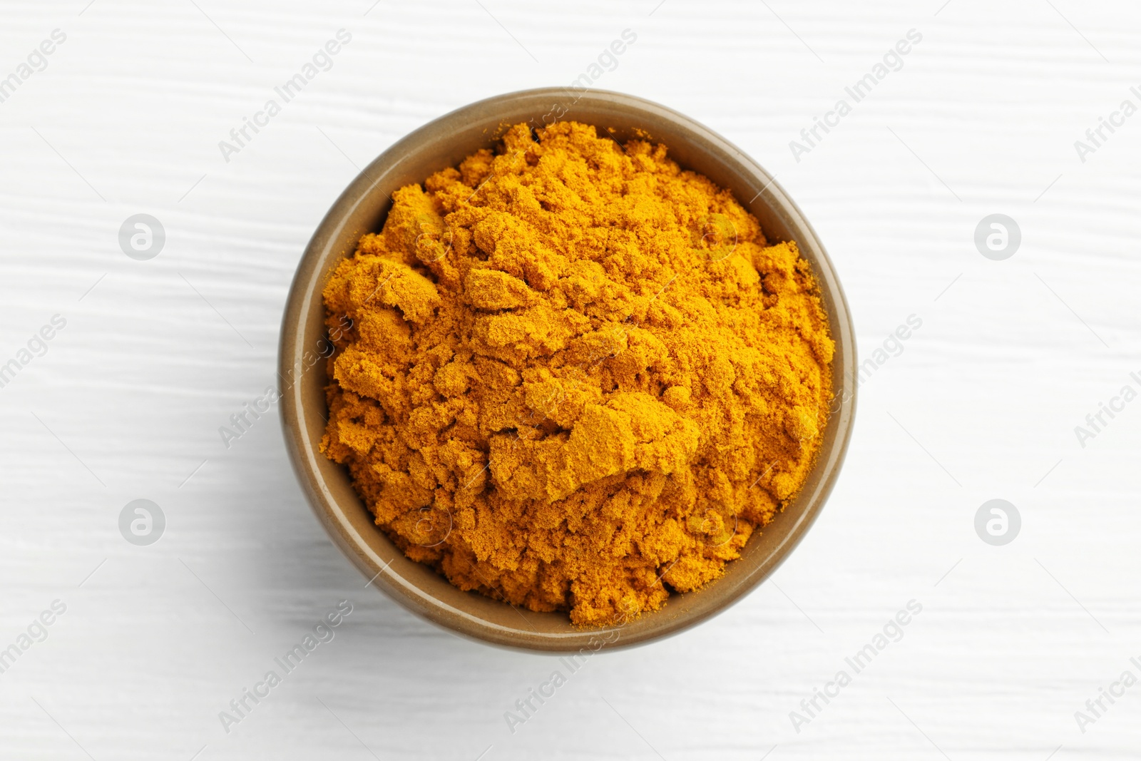 Photo of Turmeric powder in bowl on white wooden table, top view