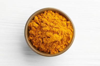 Photo of Turmeric powder in bowl on white wooden table, top view