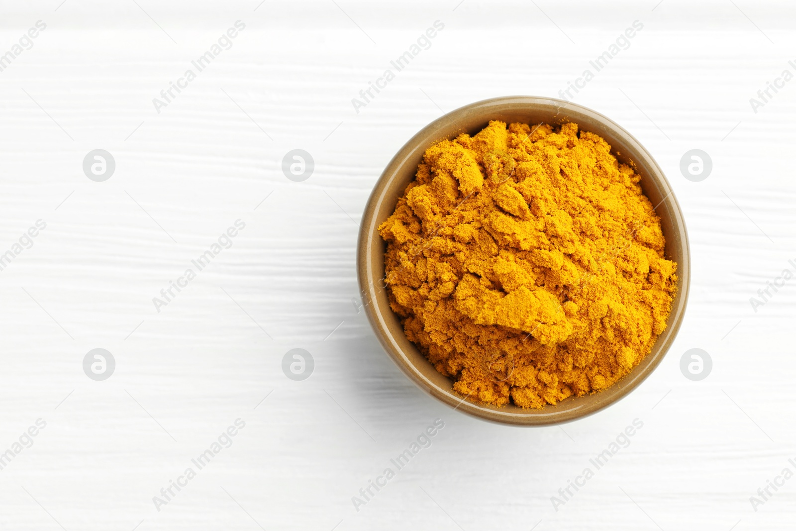 Photo of Turmeric powder in bowl on white wooden table, top view. Space for text