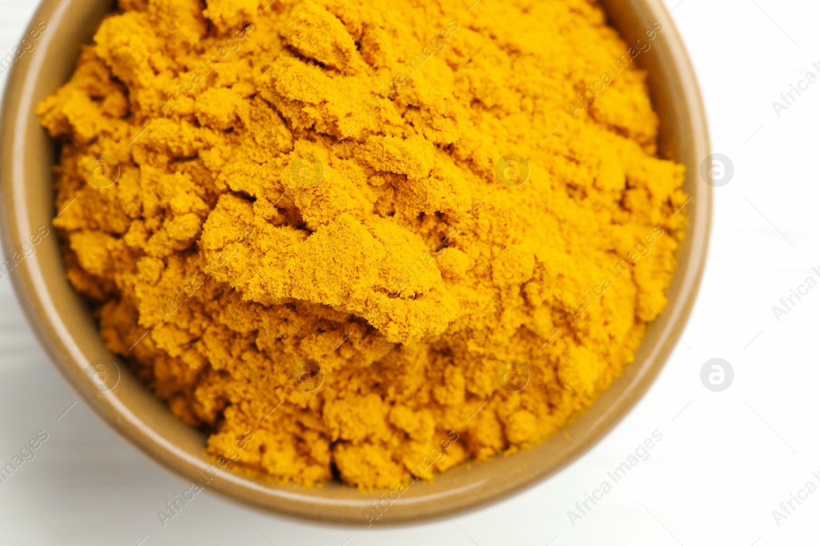 Photo of Turmeric powder in bowl on white wooden table, closeup. Top view