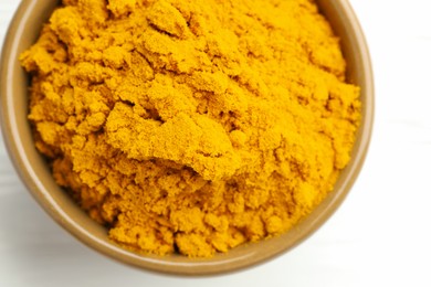 Photo of Turmeric powder in bowl on white wooden table, closeup. Top view