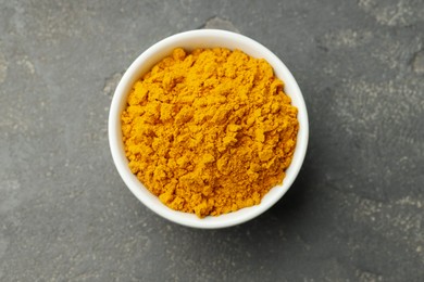 Photo of Turmeric powder in bowl on grey table, top view