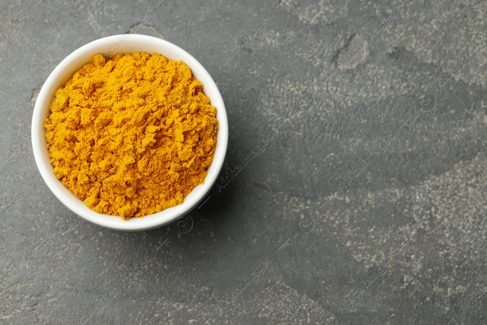 Photo of Turmeric powder in bowl on grey table, top view. Space for text