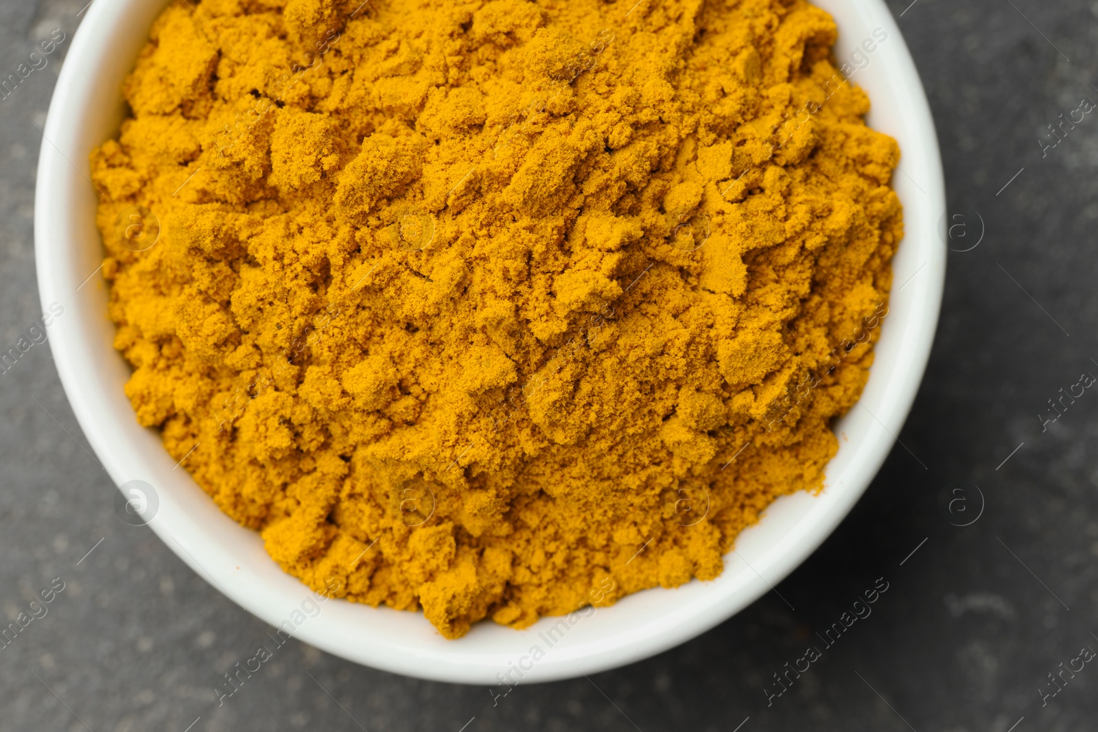 Photo of Turmeric powder in bowl on grey table, top view