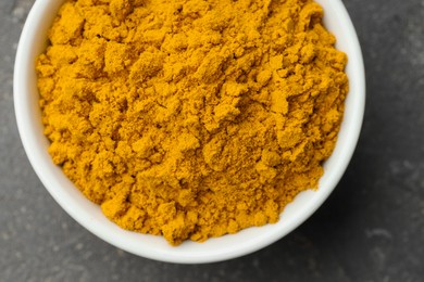 Photo of Turmeric powder in bowl on grey table, top view