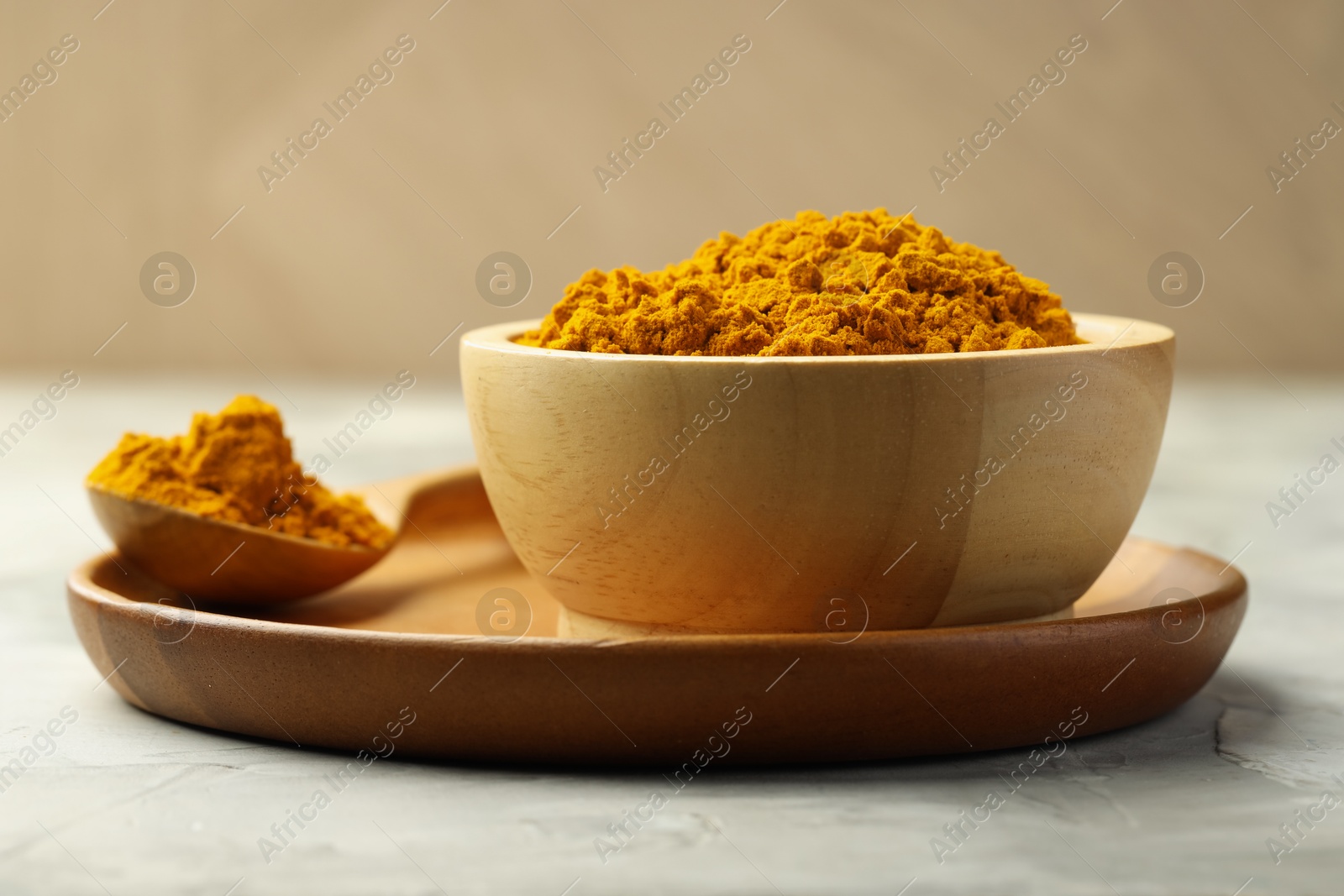 Photo of Turmeric powder in bowl and spoon on light grey table, closeup