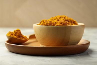 Photo of Turmeric powder in bowl and spoon on light grey table, closeup