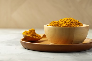 Photo of Turmeric powder in bowl and spoon on light grey table, closeup