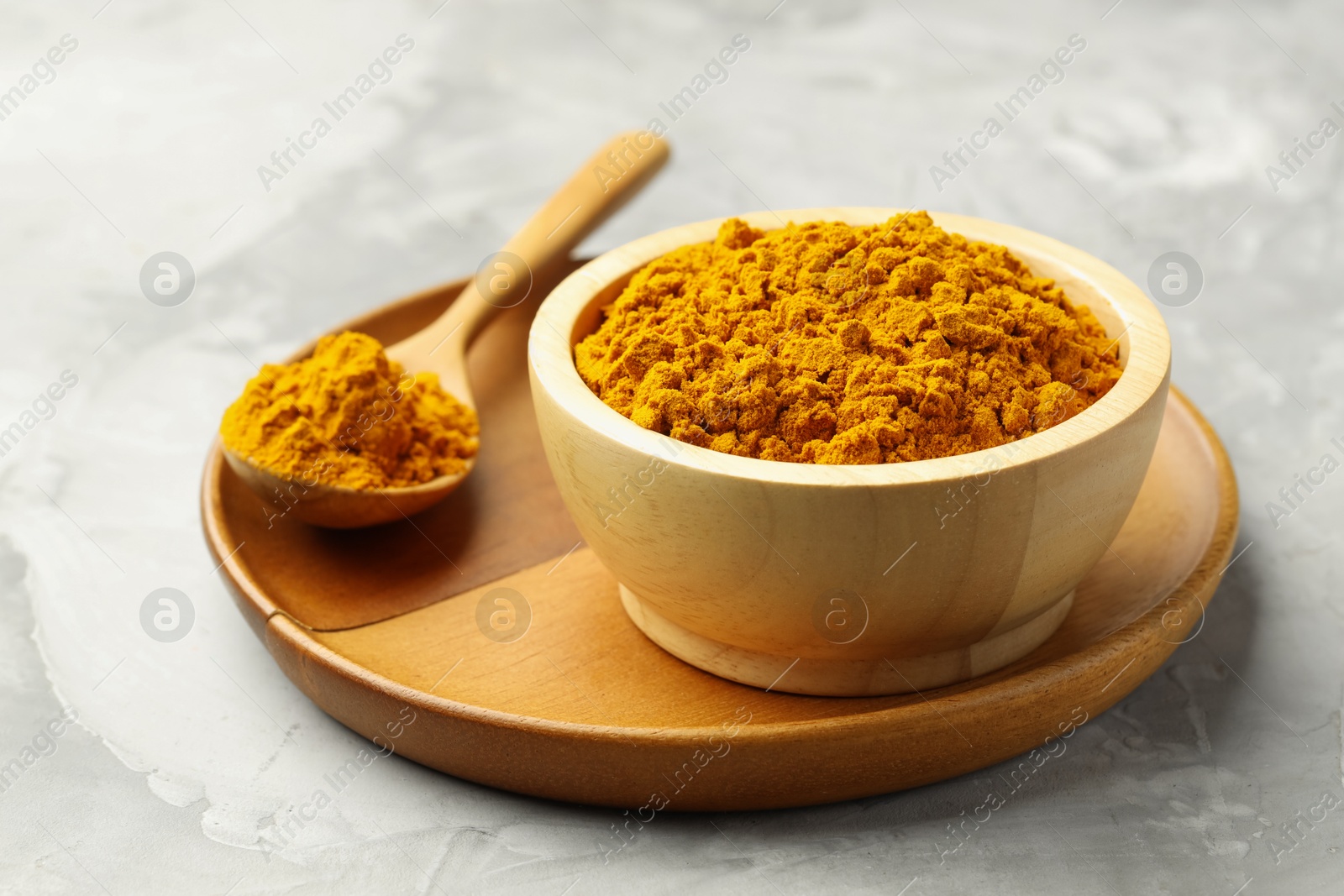 Photo of Turmeric powder in bowl and spoon on light grey table, closeup