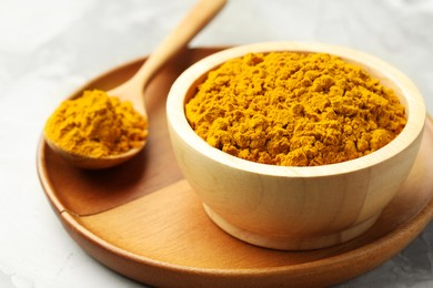 Photo of Turmeric powder in bowl and spoon on light grey table, closeup